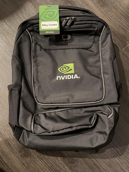 A backpack featuring an embroidered NVIDIA logo, with an NVIDIA-branded tag saying "Riley Combs" (sic).
