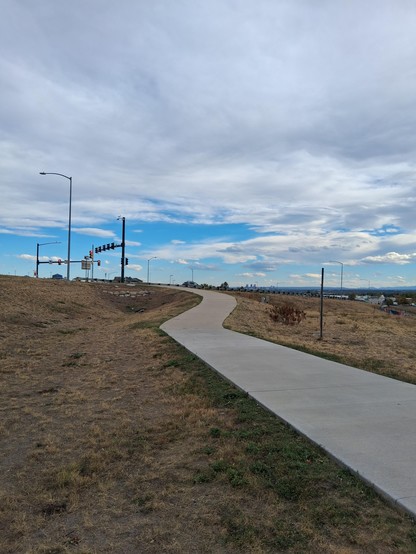 Path by highway with Denver skyline way beyond the highway below cloudy sky