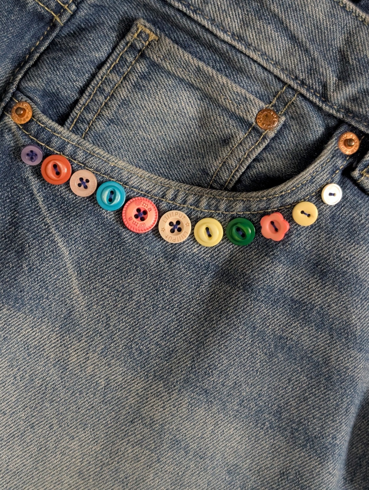 a couple of buttons sewed over the pocket edge of a lightly washed denim jeans a couple of buttons sewed over the pocket edge of a lightly washed denim jeans