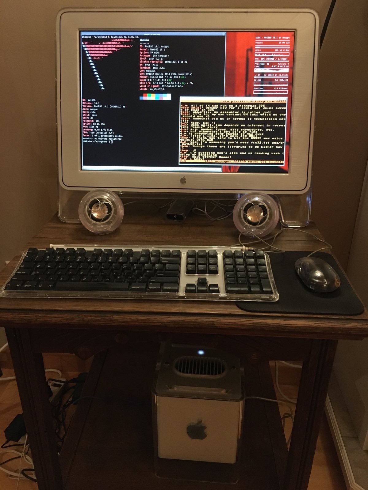 25 year old Macintosh G4 cube running a current release of NetBSD. the cube is below a wooden desk that also features the original mac display, keyboard, mouse, and small spherical speakers.