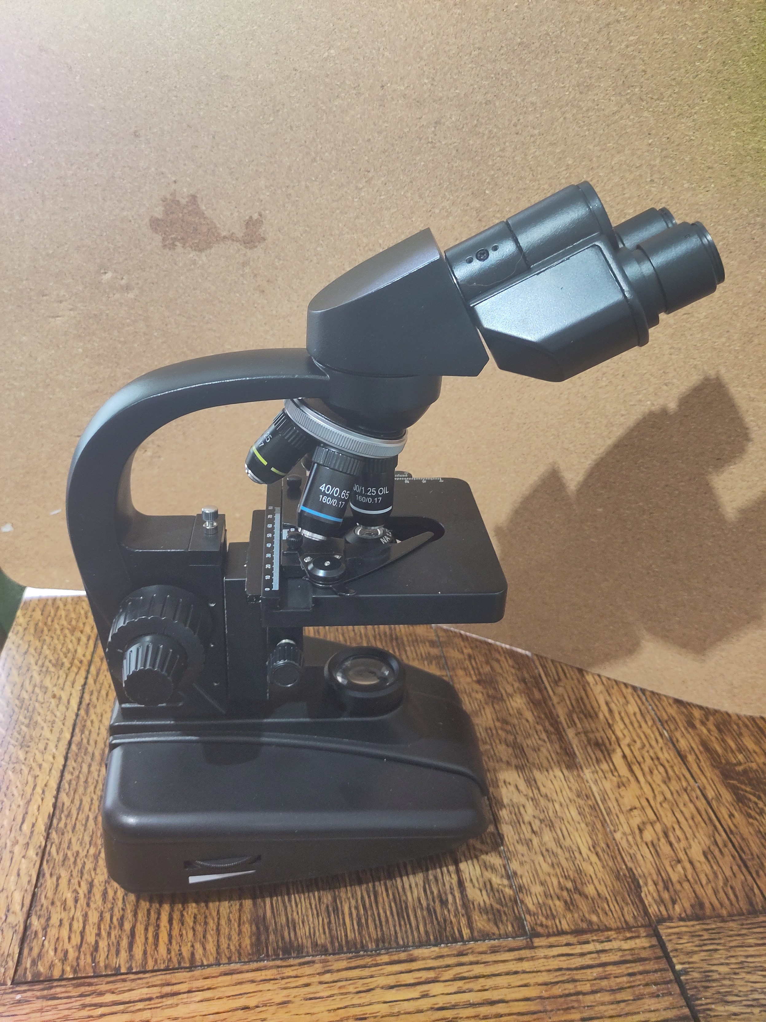 View of a black microscope from the side, includes eye pieces, objectives, plate and light