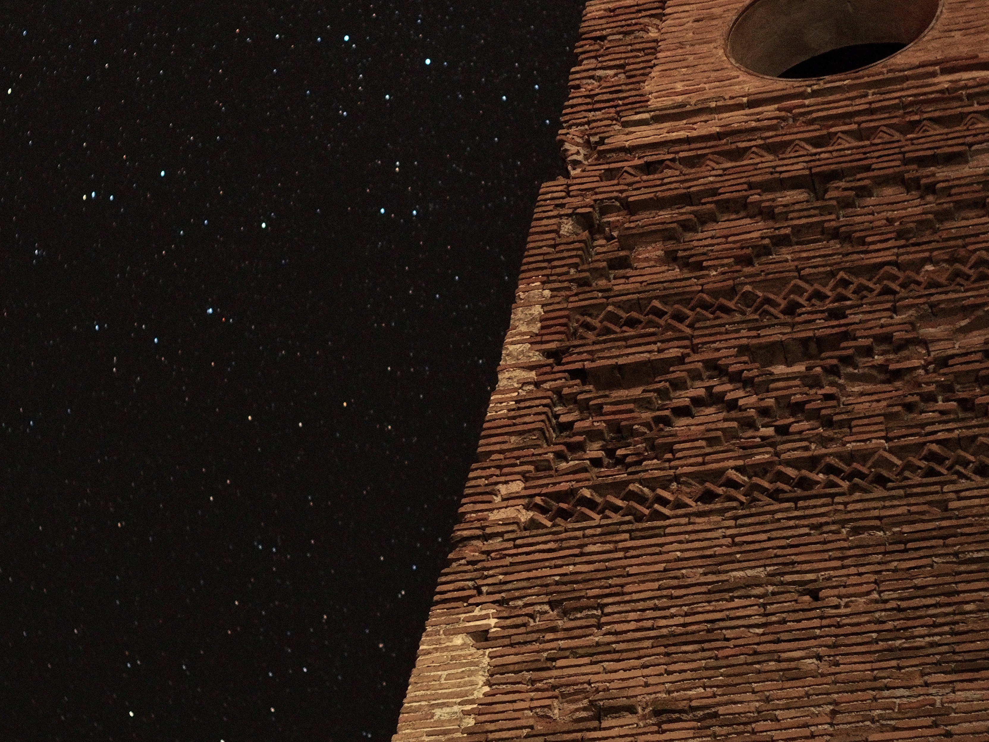 Closeup of an old brick building in ruins dividing the frame in two diagonally. Many bright stars on the background.