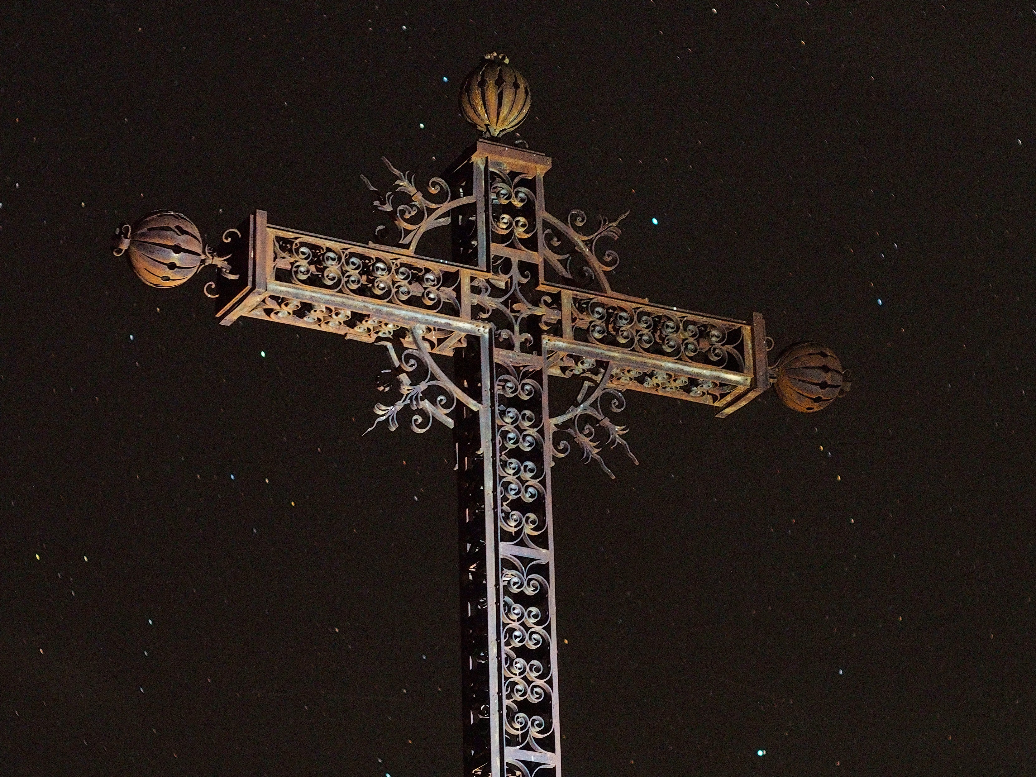 An ornate metal cross, illuminated by a lantern against the dark starry sky.