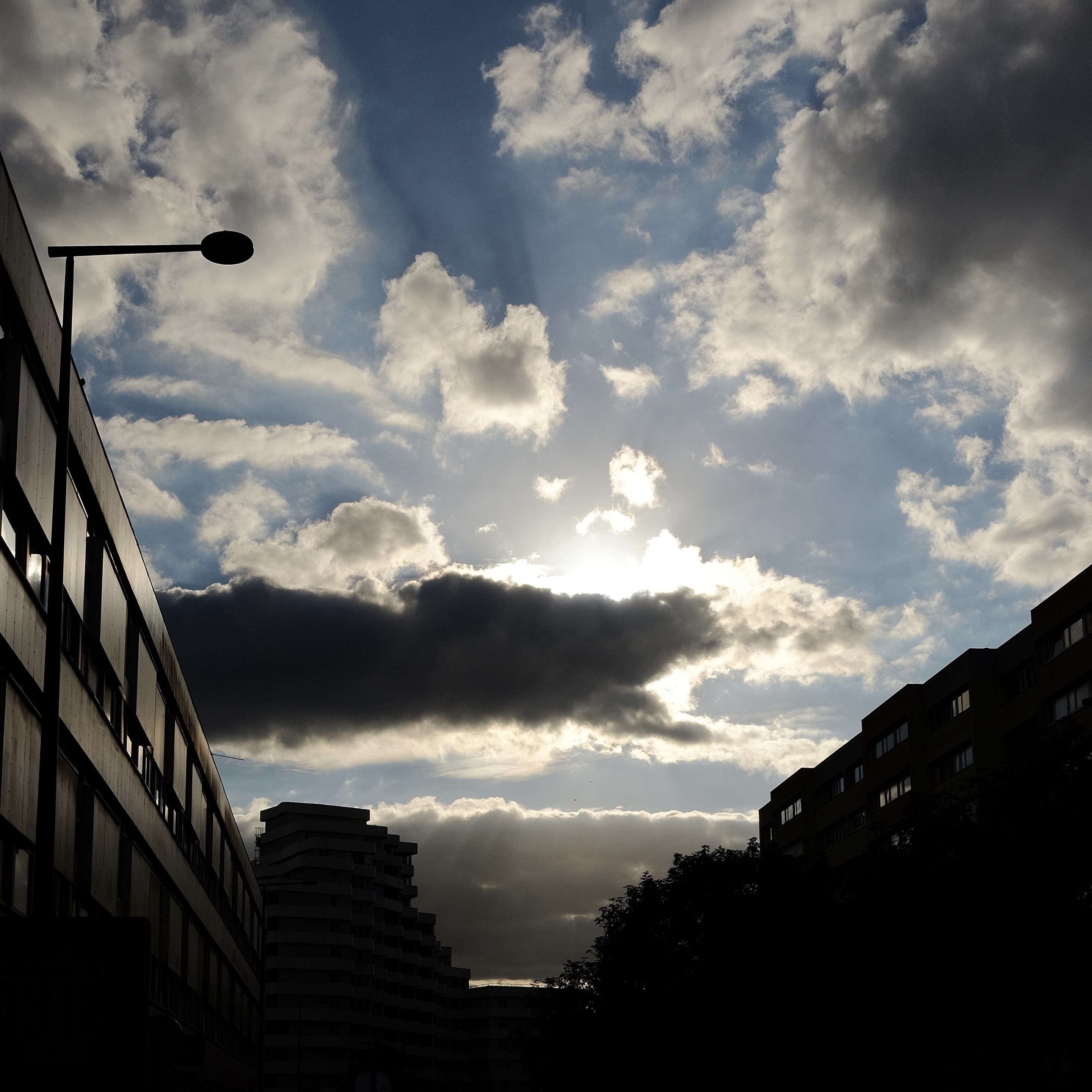 Square format.

Urban scene, with a partly cloudy sky contrasted by silhouettes of urban elements (building, lights, facades)
Light is dramatic but still retain some softness.