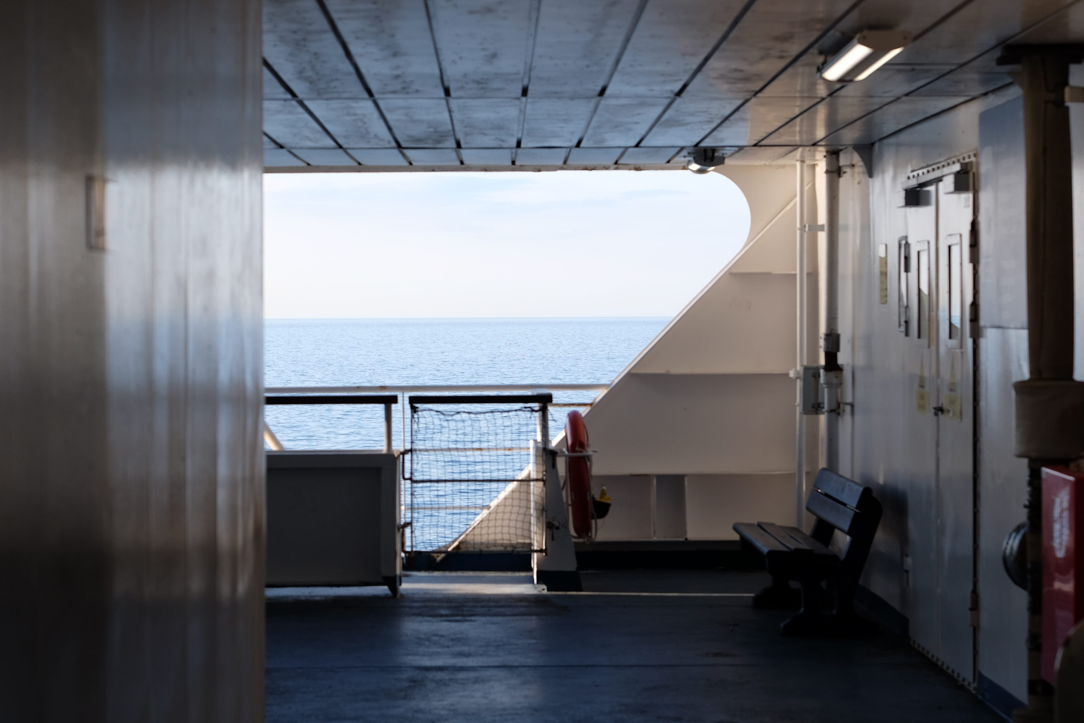 Landscape format. Ship deck.

Geometric image took from a lower deck of a ship. The walls, the ceiling, pipes, railing and hull of the ship follows harmonious lines. The sea is visible  through an diagonal opening in the hull of the boat.
Late afternoon sun, warm light.